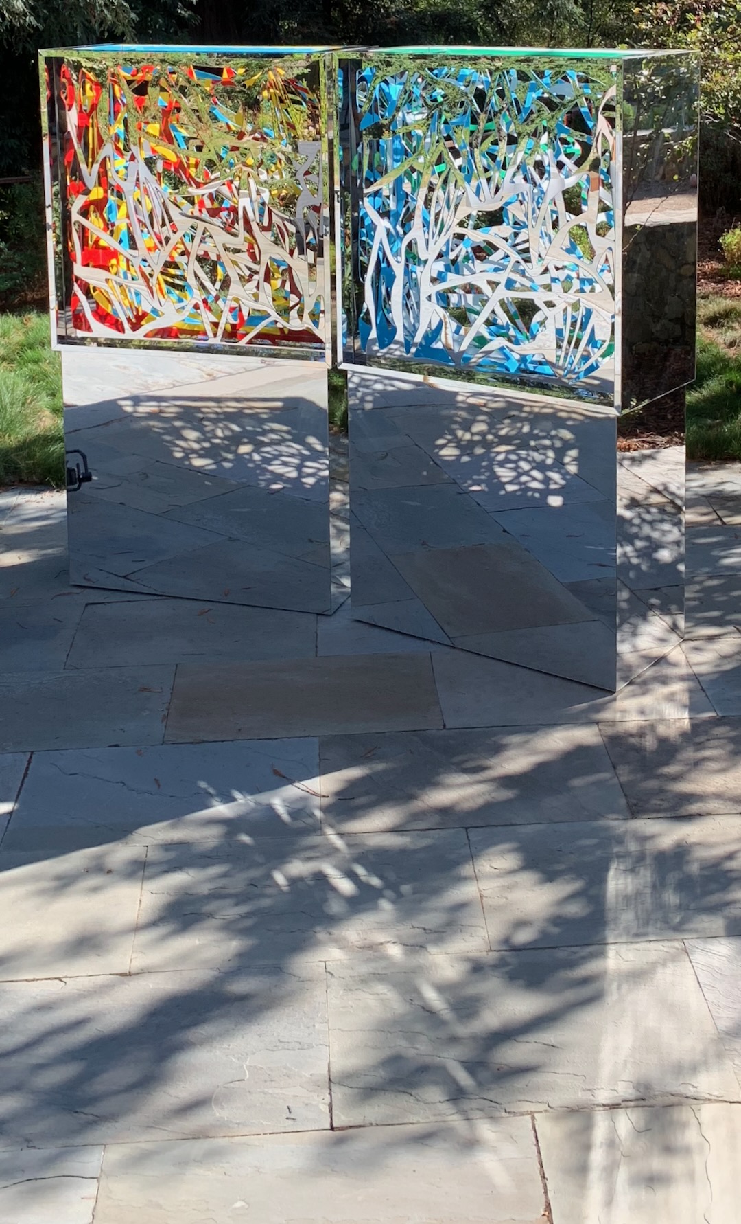 Two-panel Ambrosia in red, yellow, and blue on mirrored pedestals, reflecting a stone terrace and garden