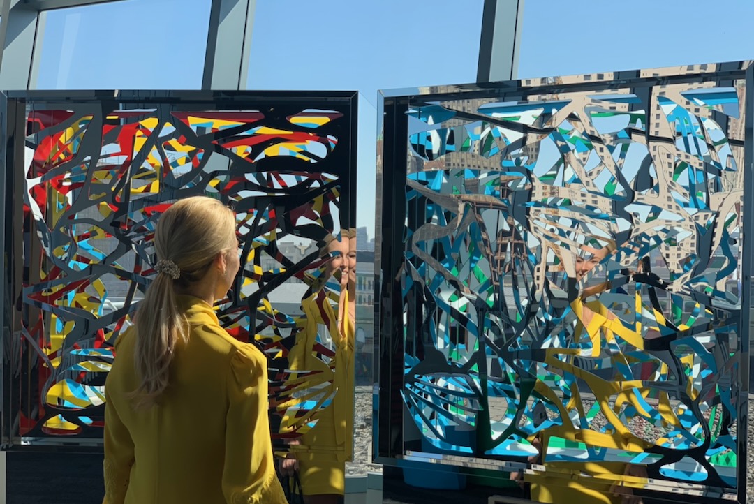 A viewer reflected between two Ambrosia panels overlooking the city skyline