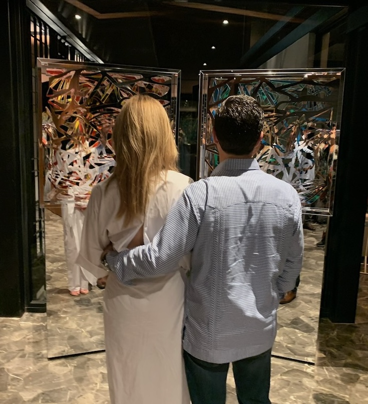 A couple standing before two mirrored Ambrosia panels in a dark interior at night