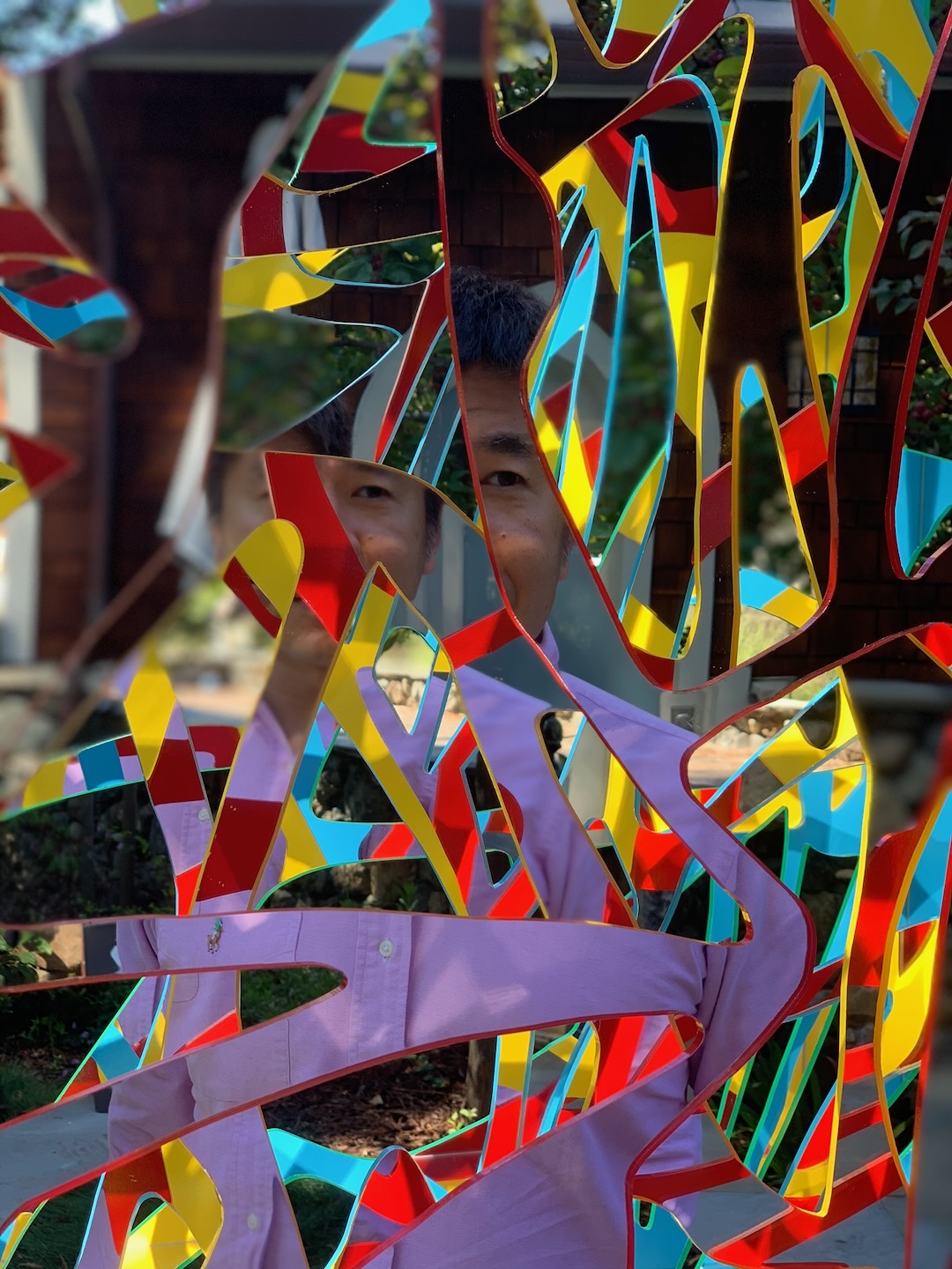 Two people peeking through a red, yellow and cyan Ambrosia panel in front of a shingled house