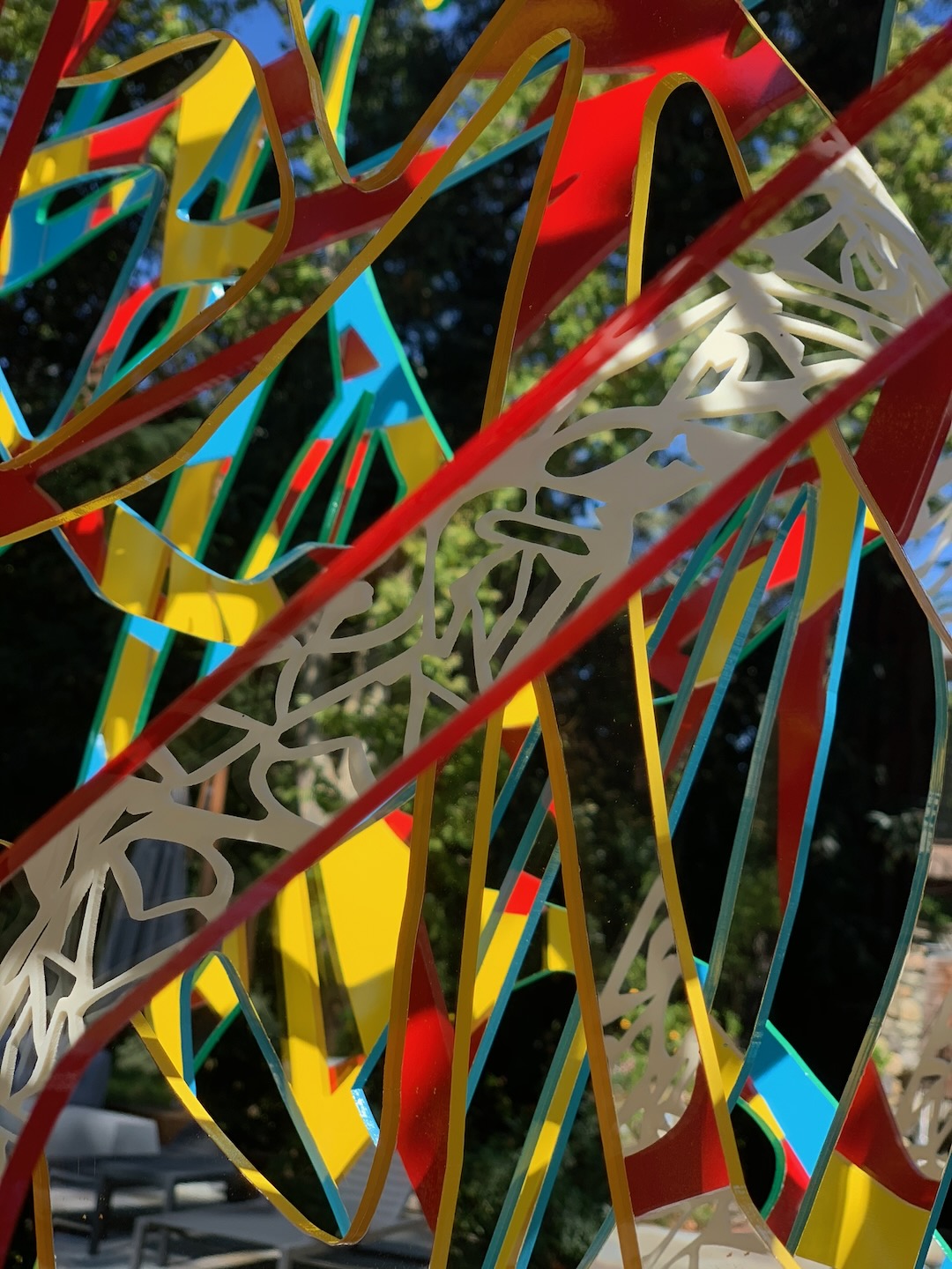 Detail of red, yellow and cyan Ambrosia ribbons with a white lattice band, trees and blue sky beyond