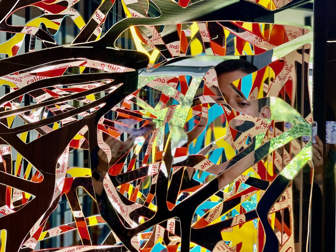 Close-up of red and yellow Ambrosia panels carrying fragments of poetry, a viewer's face appearing through the cutouts