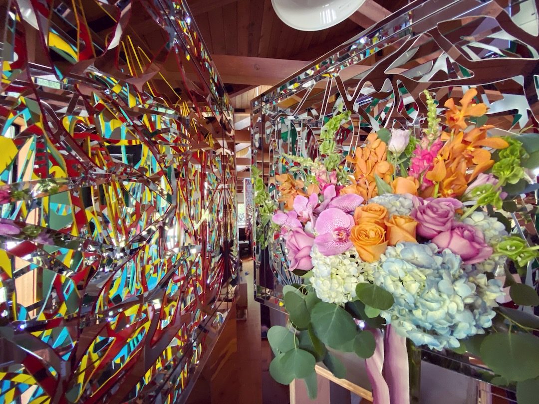 A bouquet of orchids, roses and hydrangeas beside red and yellow Ambrosia panels beneath a wood-beamed ceiling