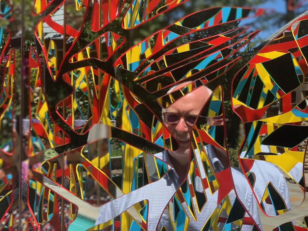 A smiling man seen through the red, yellow and cyan ribbons of an Ambrosia panel outdoors