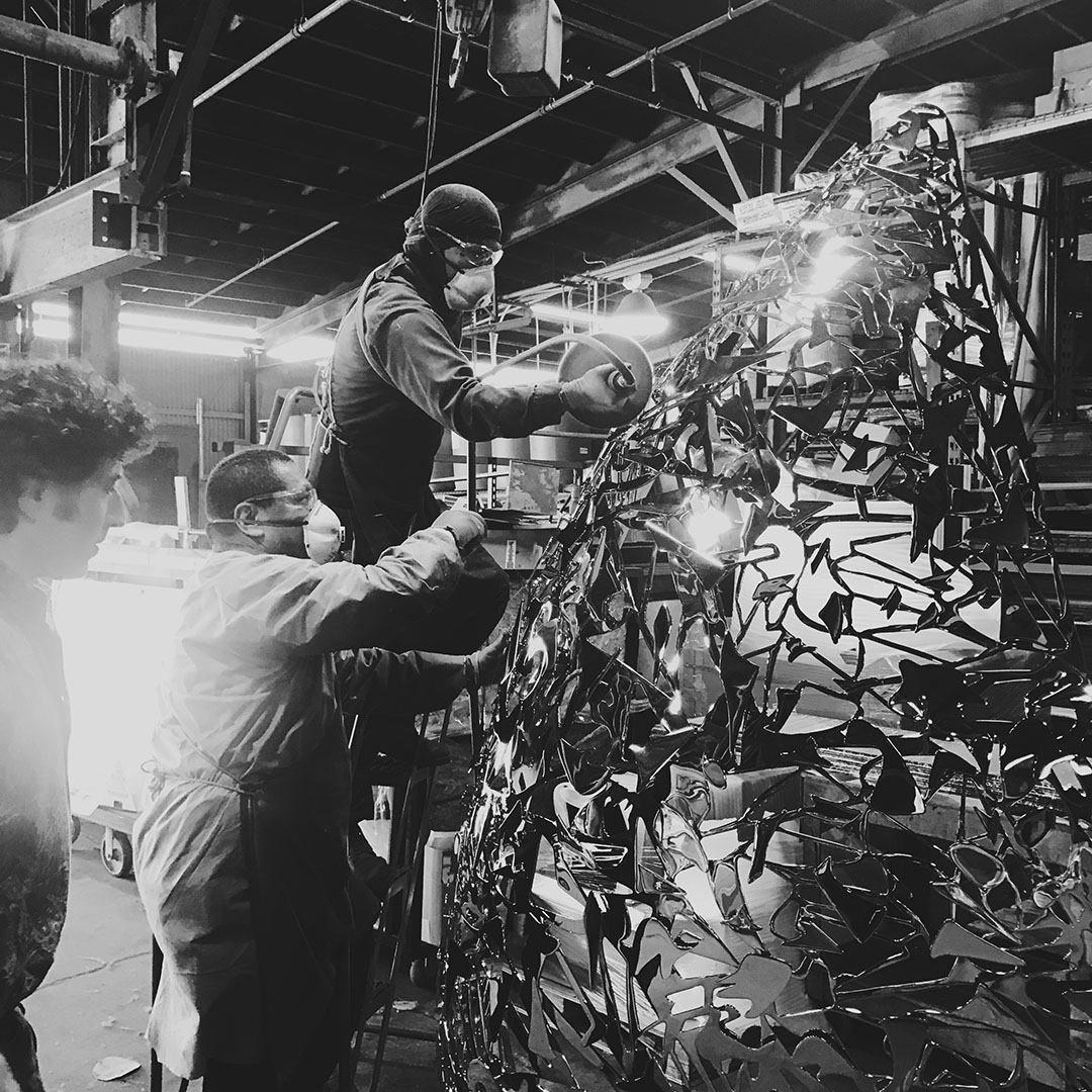 Fabricators hand-polishing a Celestial Lace lattice sculpture in the workshop, under overhead cranes and lights