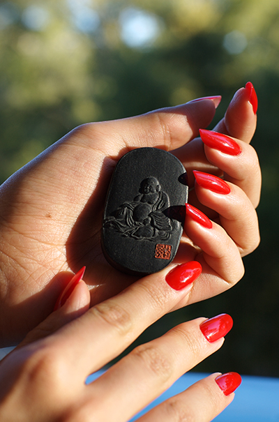 Black sumi ink stick molded with a relief of a seated Buddha and a red seal, cradled in Drue Kataoka's hand