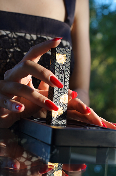 Drue Kataoka's hands holding a gold-leafed sumi ink stick upright over a black suzuri inkstone